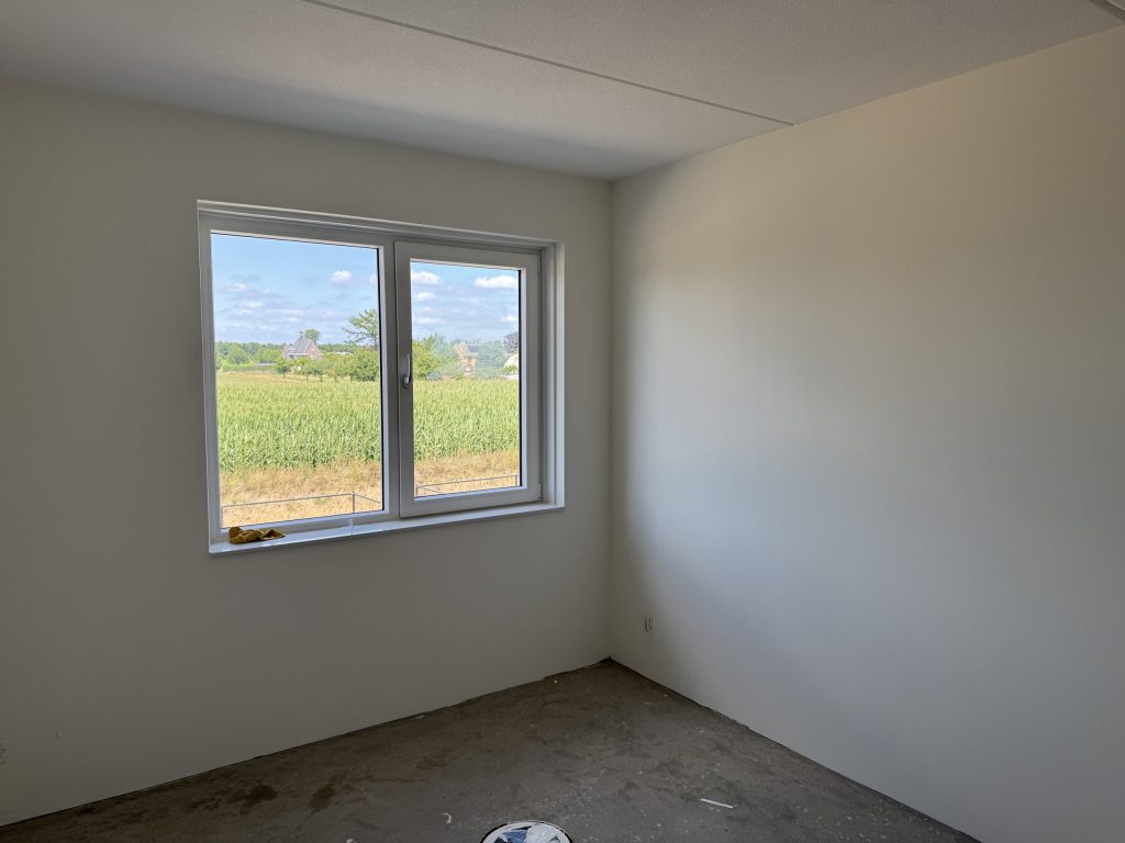 Lege kamer met gladde, lichte wanden en een raam met uitzicht op een akker